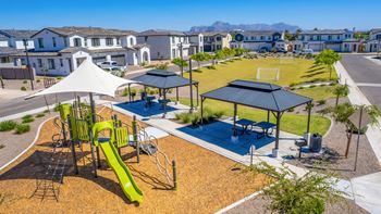 a playground with a slide and picnic tables in front of houses